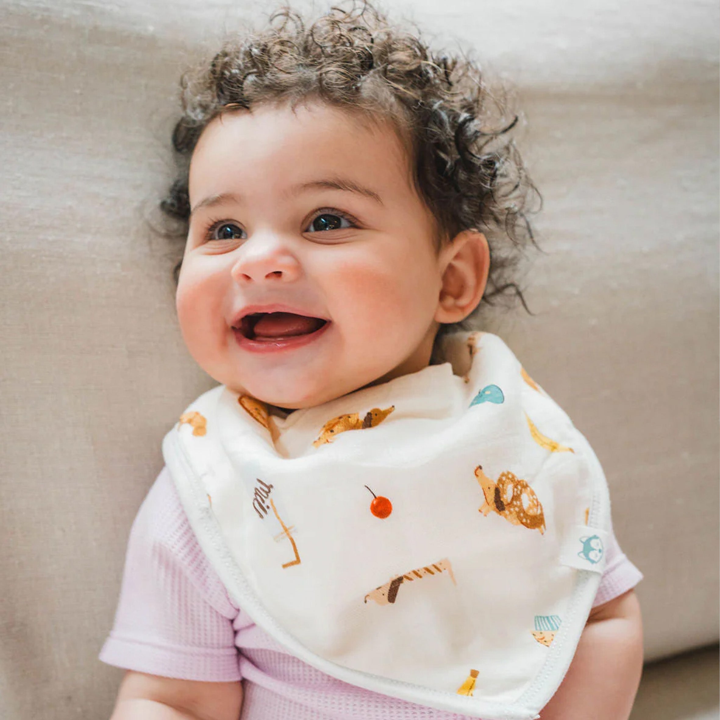 Baby wearing a French Breakfast Bandana Bib, sitting on a couch