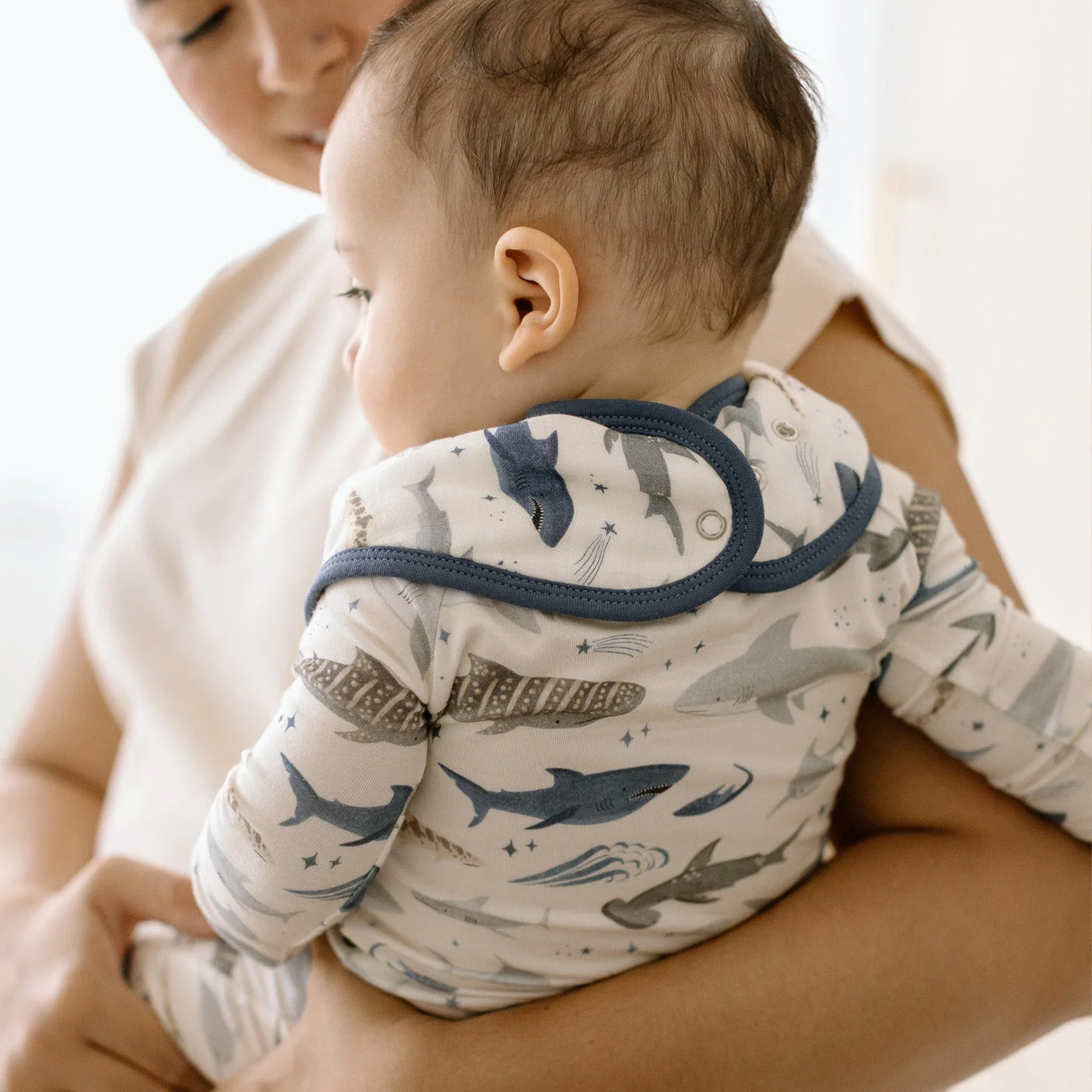 A baby wearing a Smiley Sharks Bandana Bib held by an adult