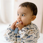 Baby wearing a Smiley Shark Long Sleeve Bib, holding a Sarah Shark Learning Utensil