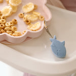Skylar Shell Snack Plate with cereal and banana slices on a white surface, with a Sarah Shark Learning Utensil spoon