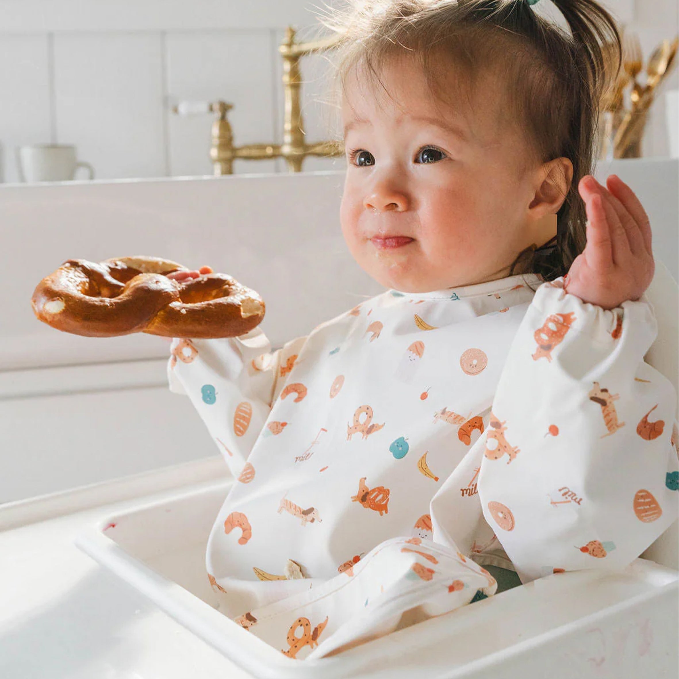 Child on a highchair wearing a French Breakfast Long Sleeve Bib
