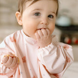 Baby in a Sea Shells Long Sleeve Bib with a soft focus background