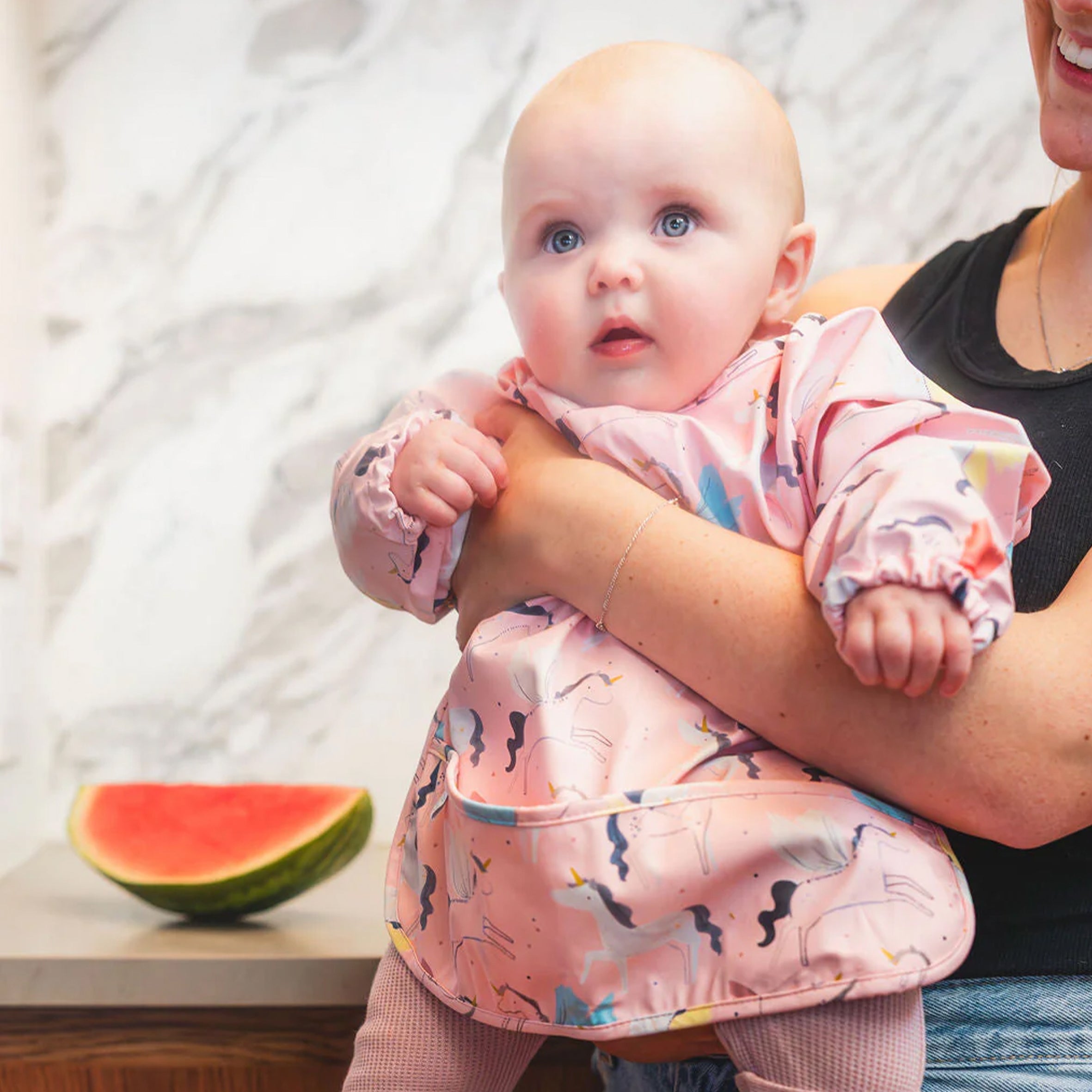 Baby in a Unicorn Ballet Long Sleeve Bib held by an adult, with a watermelon in the background