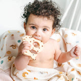 Baby holding a Cookie Dog teething Charm on a French Breakfast Muslin Swaddle