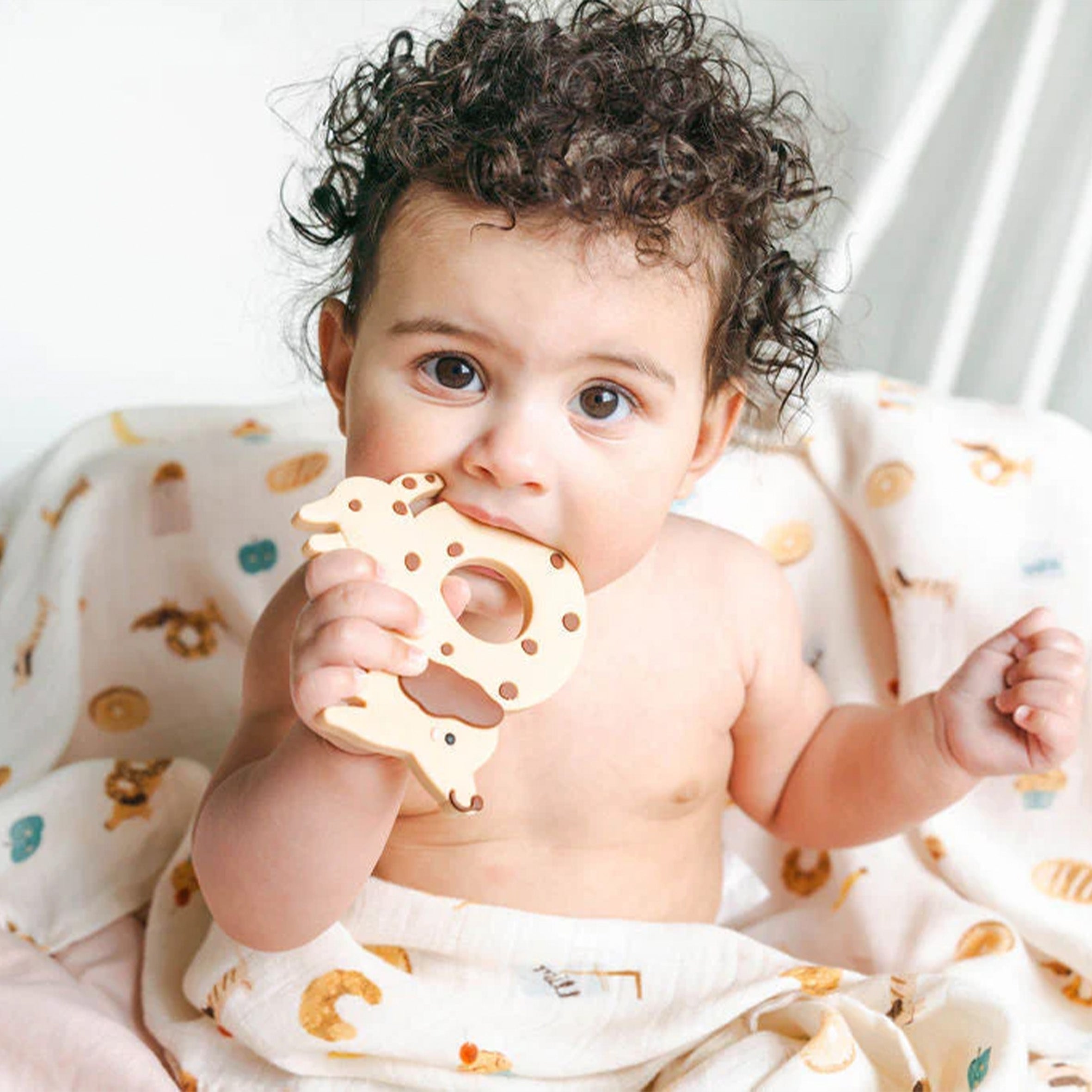 Baby holding a Cookie Dog teething Charm on a French Breakfast Muslin Swaddle