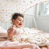 Baby laughing in a crib with a French Breakfast Muslin Swaddle as a canopy