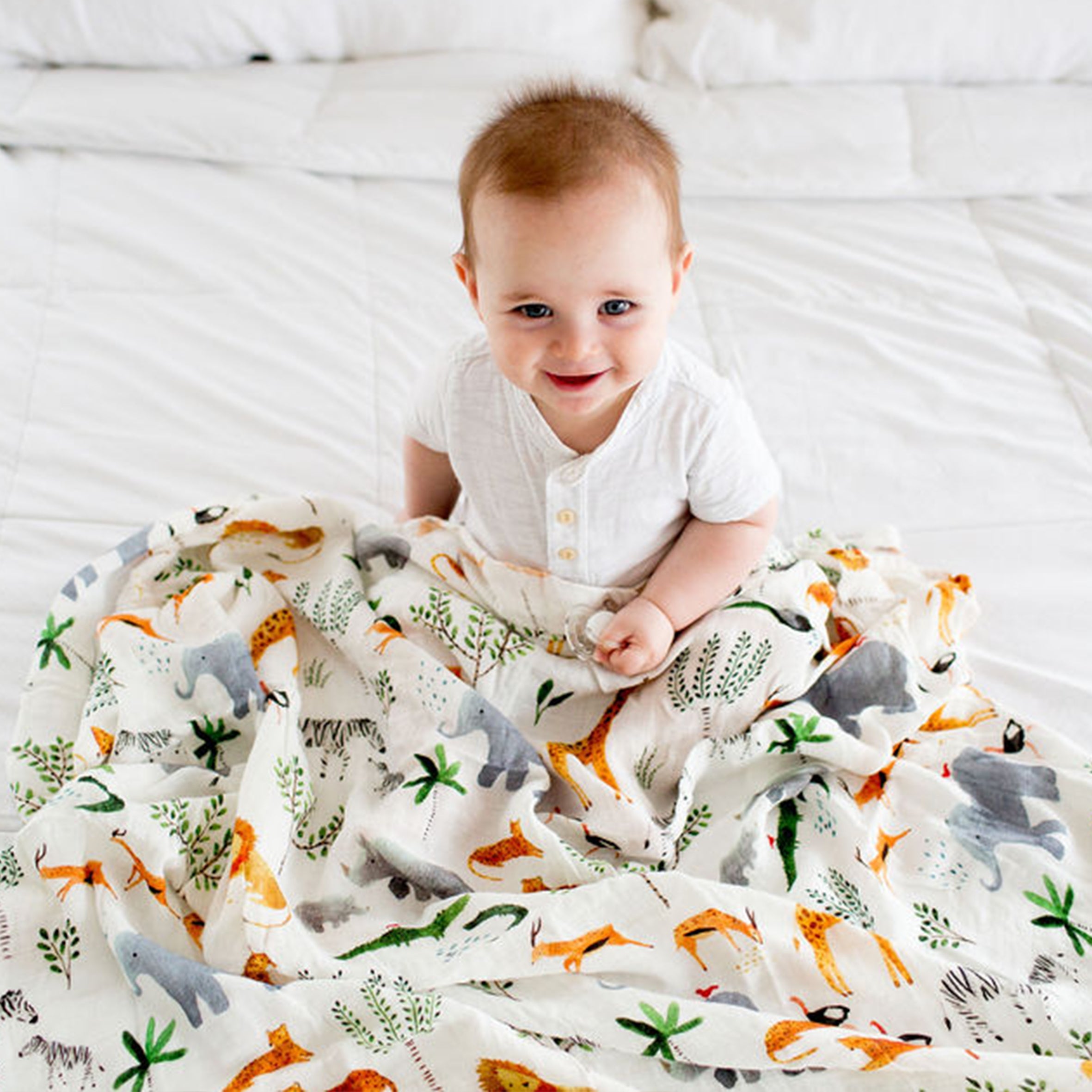 Baby sitting on a Safari Jungle Muslin Swaddle, wearing a white shirt.