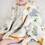 Baby wrapped in a Safari Jungle Muslin Swaddle on a neutral background