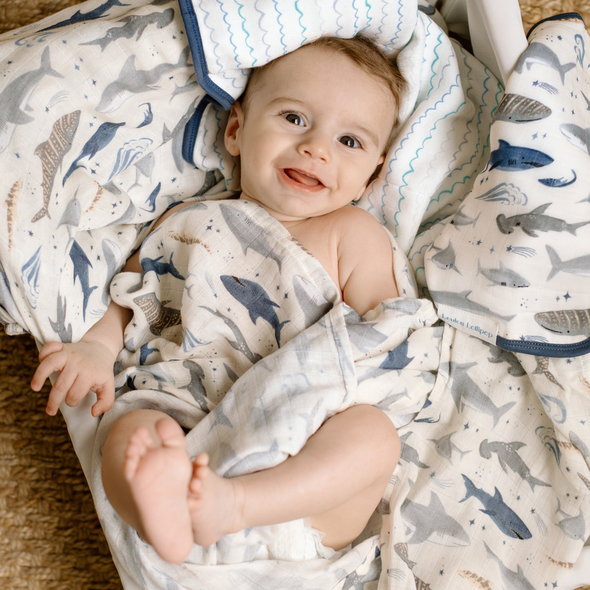 Baby wrapped in a Smiley Sharks Muslin Swaddle, lying on a soft surface