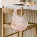 Sea Shell Silicone bib hanging on a wooden chair in a kitchen setting