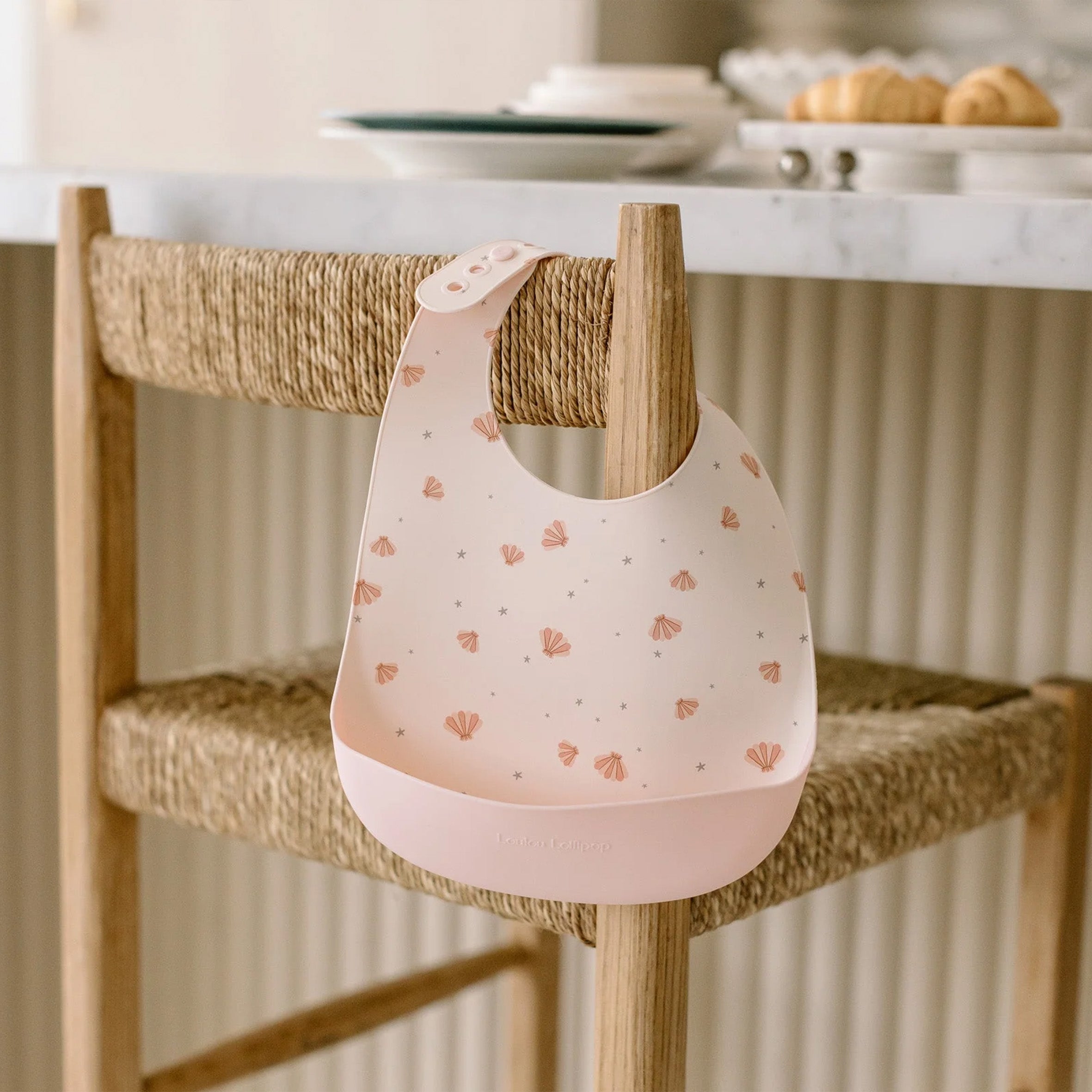 Sea Shell Silicone bib hanging on a wooden chair in a kitchen setting