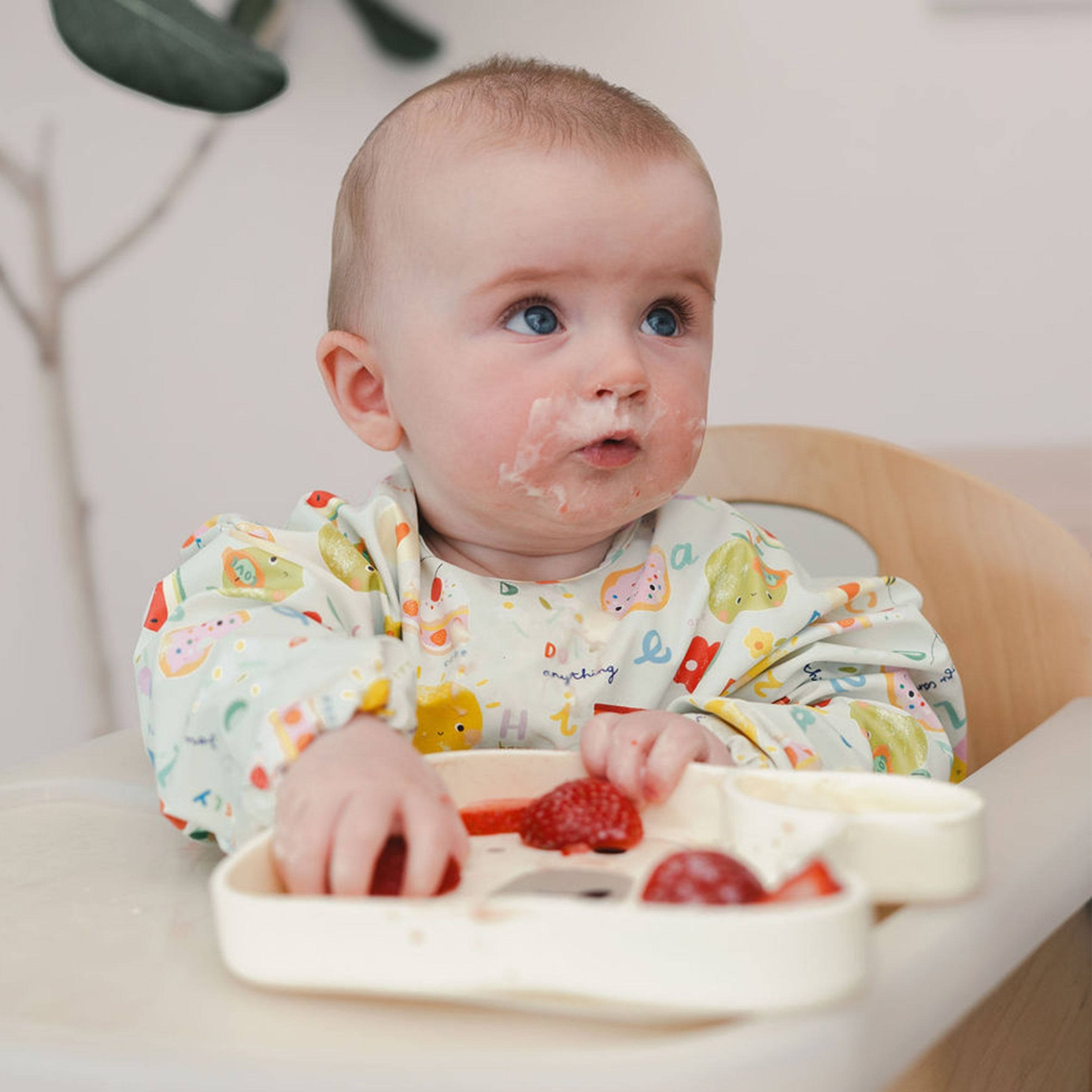 Baby in a high chair with a plate of food eating off a Lane Llama Snack Plate