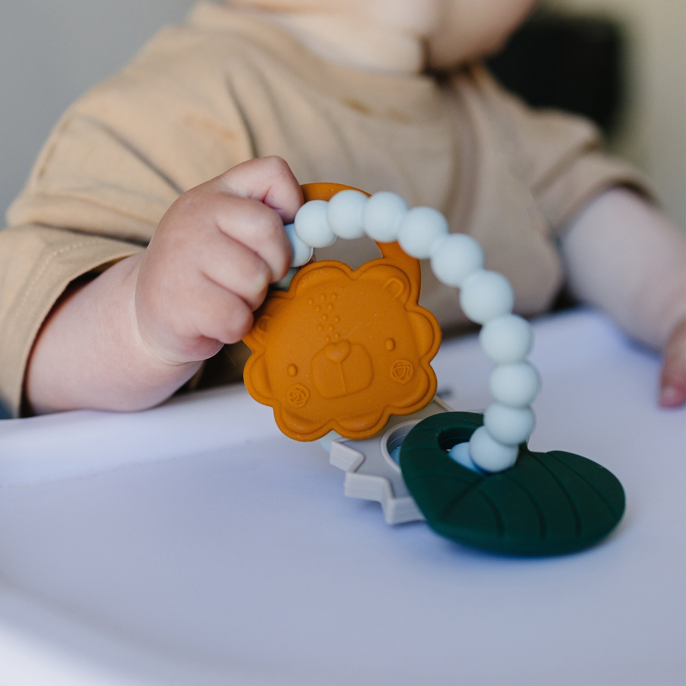 Baby holding a Liam Lion teething charms with a blurred background