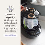 A person places a bottle accessory into the Baby Brezza Bottle Washer Pro® - All Black, filled with bottles and parts. Text: Universal capacity—washes up to 4 bottles, sippy cups, pump parts & accessories from any brand.