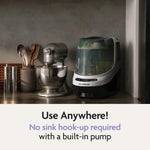 The Baby Brezza Bottle Washer Pro® - All Black sits beside a stand mixer and utensils. Text below reads: Use Anywhere! No sink hook-up needed thanks to the built-in pump on this automatic bottle cleaner by Baby Brezza.