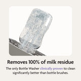 The Baby Brezza Bottle Washer Pro® - All Black cleans a clear baby bottle upside down with water jets. Text: “Removes 100% of milk residue. The only Bottle Washer clinically proven to clean better than bottle brushes.”.