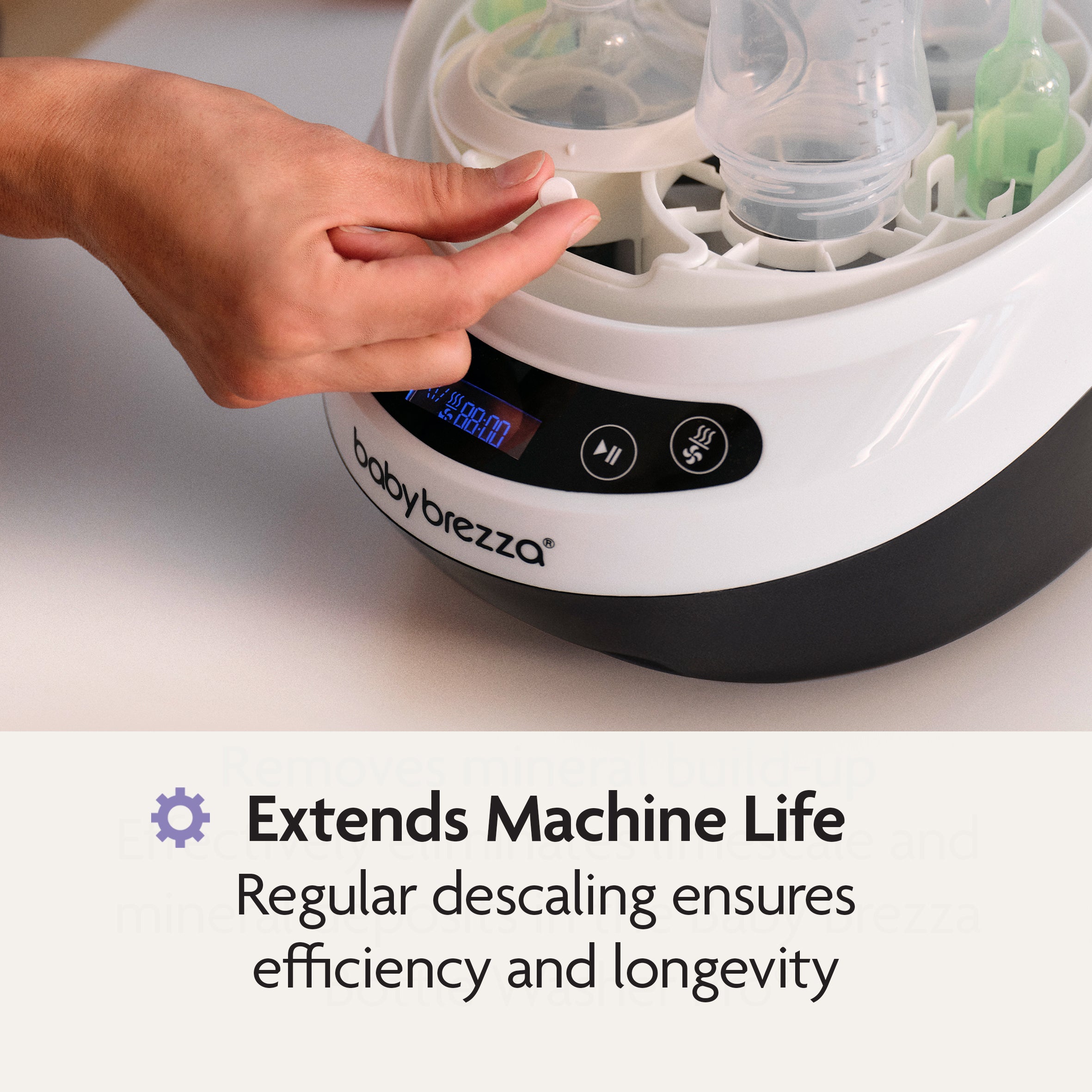 A hand places a Baby Brezza Bottle Washer Pro Descaling Tablet into the bottle washer to remove limescale and ensure machine efficiency.