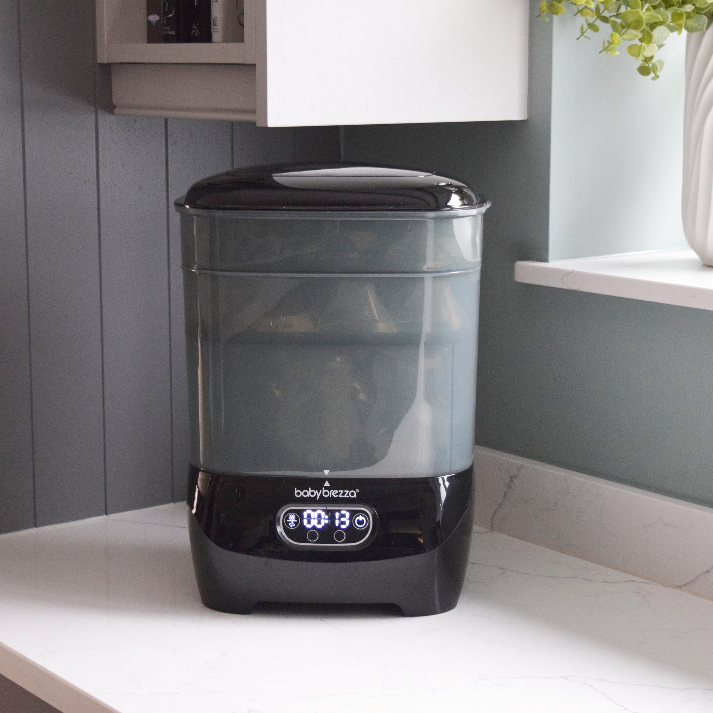 Black and translucent grey PRE-LOVED: Baby Brezza Steriliser Dryer Advanced - All Black with a digital display reading 00:13 on a kitchen counter.