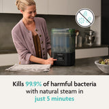 A smiling woman uses the Baby Brezza SuperQuick Steriliser Dryer in a modern kitchen. Text: Kills 99.9% of harmful bacteria with natural steam in just 5 minutes. Features largest capacity for easy, effortless sanitizing. Brand: Baby Brezza.