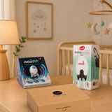 A softly lit nursery showcases the Cheeky Rascals UK Newborn Essentials Bundle—featuring the Rockit Wooshh, baby rocker, and Izmi Essential Wrap—ideal for expecting parents or as a thoughtful Baby Shower gift.
