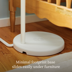 A circular white Owlet Dream Sight™ Camera Stand base slid underneath a wooden crib.