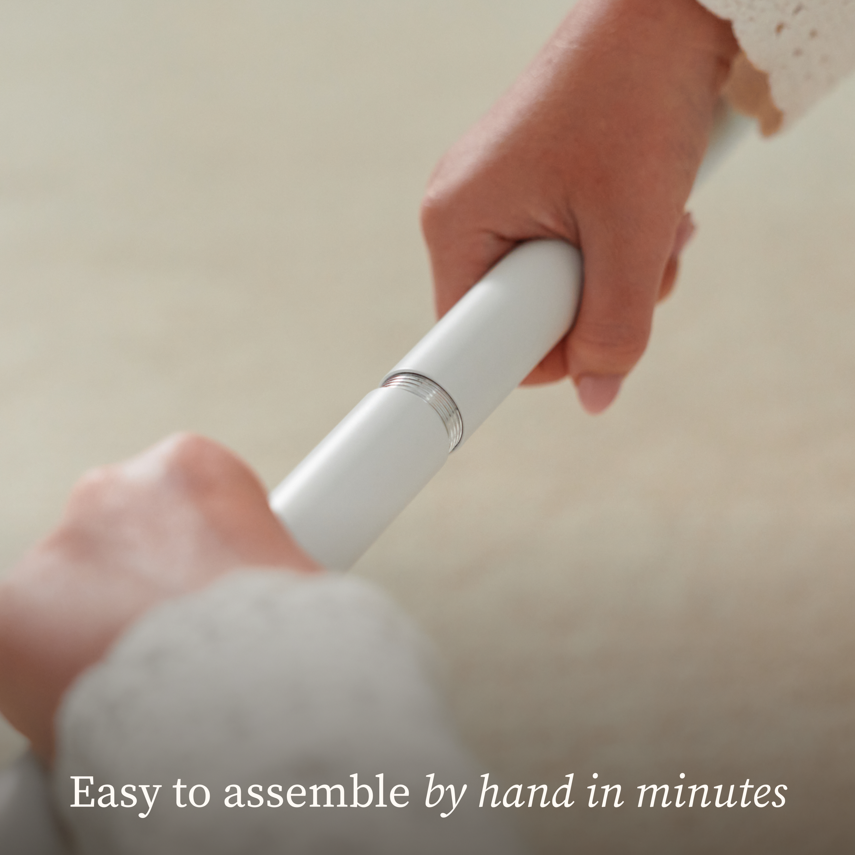 Hands assembling two sections of a white Owlet Dream Sight™ Camera Stand, with text overlay reading, Easy to assemble by hand in minutes.
