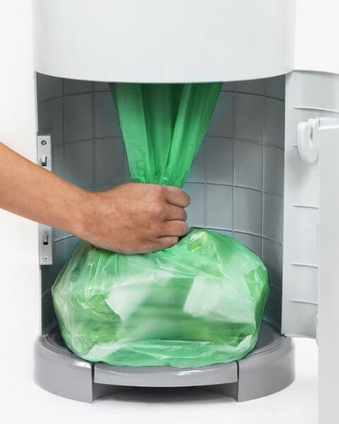 A hand places a full green trash bag inside an open, grey Korbell Nappy Bin with a tiled interior, demonstrating the convenience of using Korbell Nappy Bin Replacement Liners – Pack of 3.