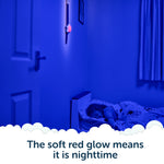 A child sleeps in bed while the Rockit Rising Star rewarding sleep clock rests beside them, its soft red nightlight glowing on the wall. The room is dimly lit with a soothing blue hue. Text reads, “The soft red glow means it is nighttime.”.