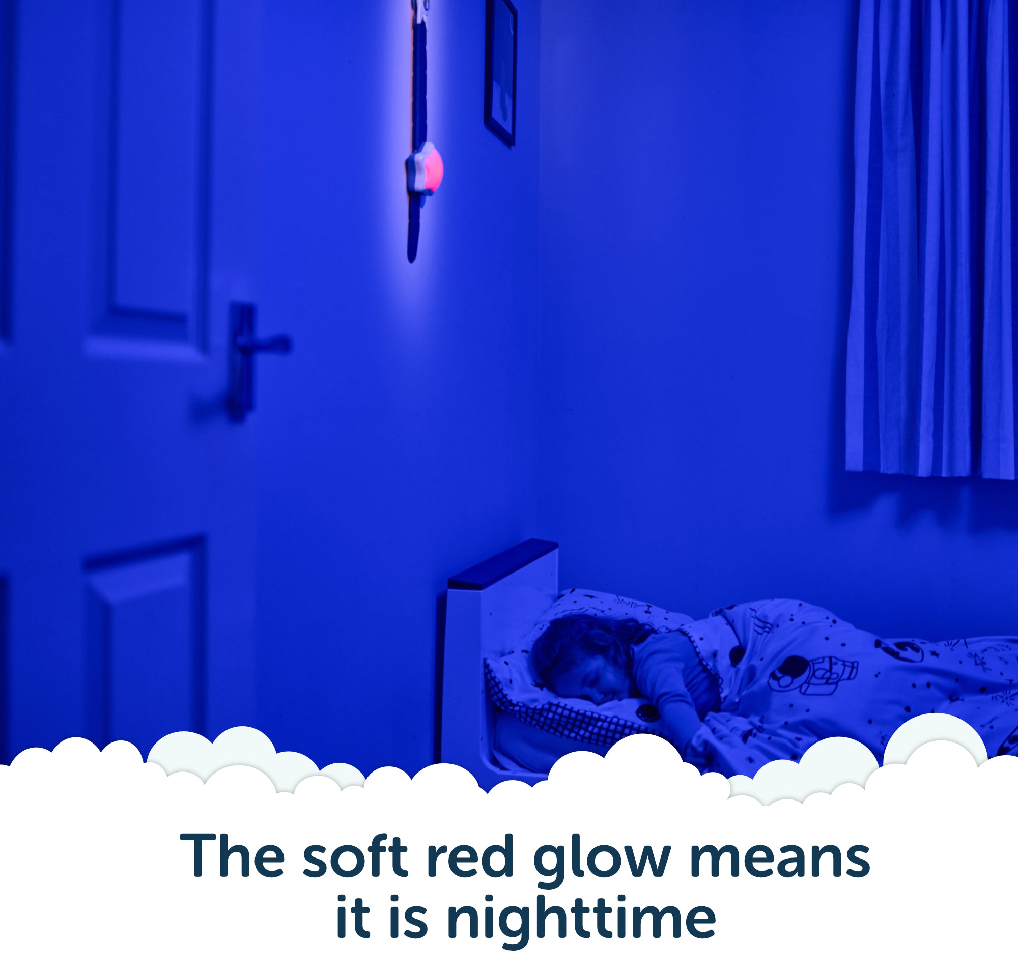 A child sleeps in bed while the Rockit Rising Star rewarding sleep clock rests beside them, its soft red nightlight glowing on the wall. The room is dimly lit with a soothing blue hue. Text reads, “The soft red glow means it is nighttime.”.
