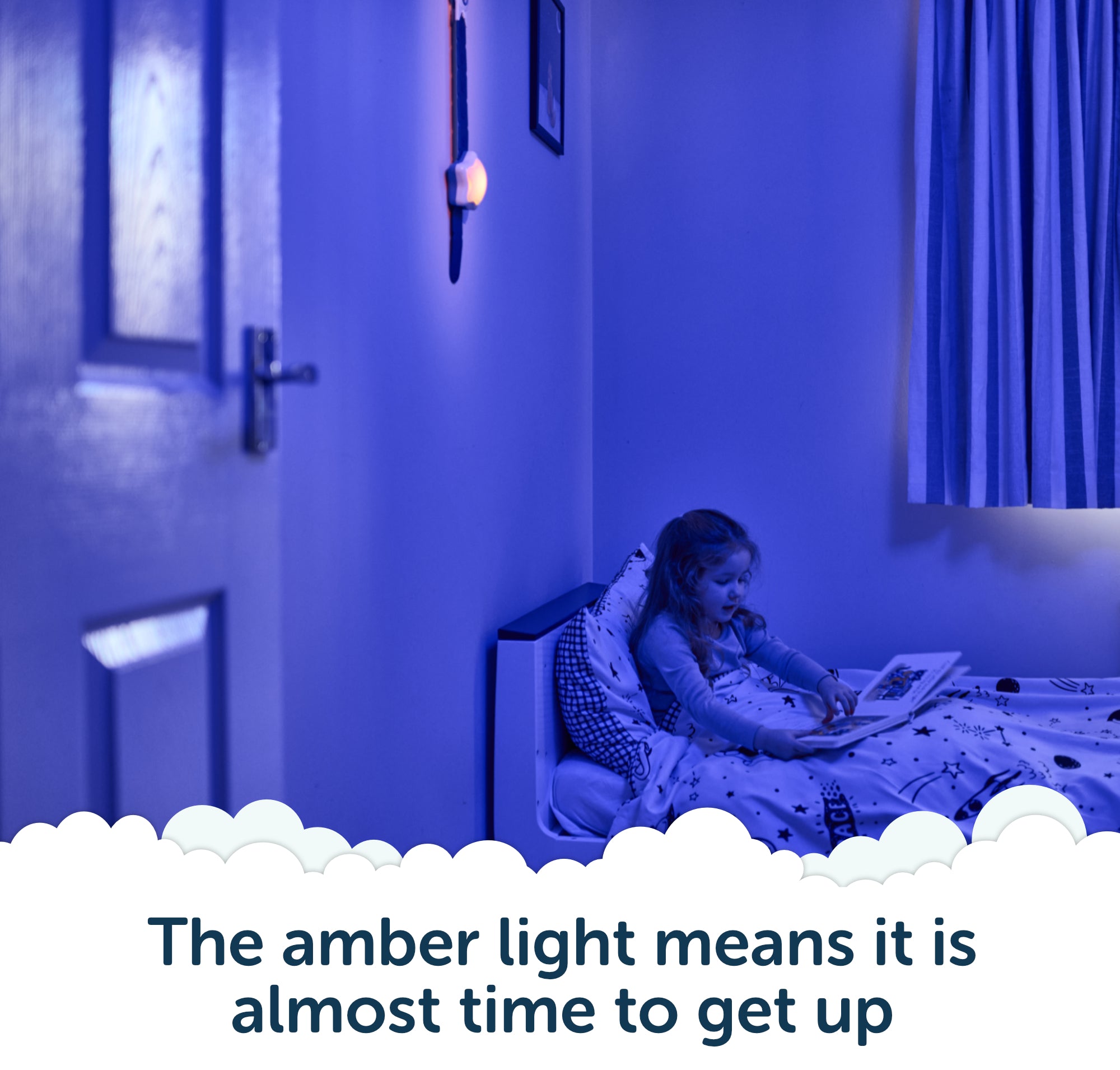 A child sits in bed under blue light, reading a book while an amber nightlight glows on the wall beneath Rockit’s Rising Star – The Rewarding Sleep Clock. Text reads: The amber light means it’s almost time to get up—thanks to this kids’ sleep trainer, mornings are easier for everyone.
