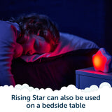 A child sleeps in bed beside a glowing star-shaped night light and Rockit’s Rising Star – The Rewarding Sleep Clock on the bedside table. Text reads, Rising Star can also be used on a bedside table.