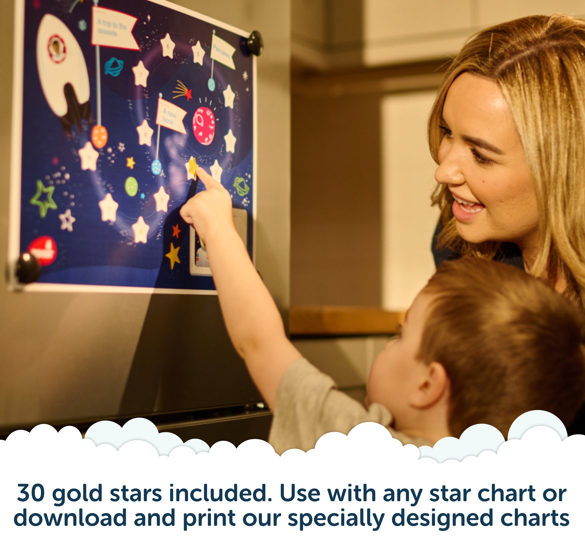 A woman and child smile and point at a space-themed star chart on a fridge. Text below says, 30 gold stars included. Use with any star chart or with the Rising Star – The rewarding sleep clock by Rockit, or download and print our specially designed charts.